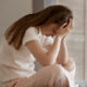 A girl sitting on a bed, worrying about depression triggers.