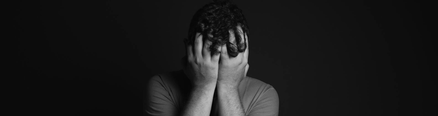 a person holding his head in his hands thinking about what triggers depression 